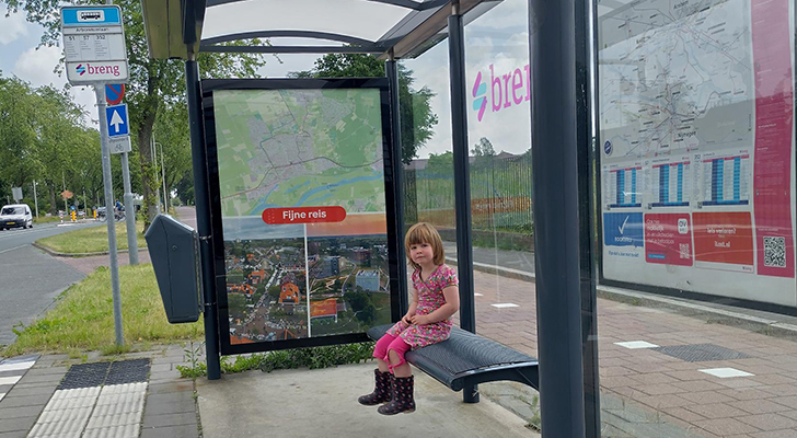 Een kind in een Wagenings bushokje. Geen ongezonde aanbiedingen, maar foto's van Wageningen met een fijne reis gewenst
